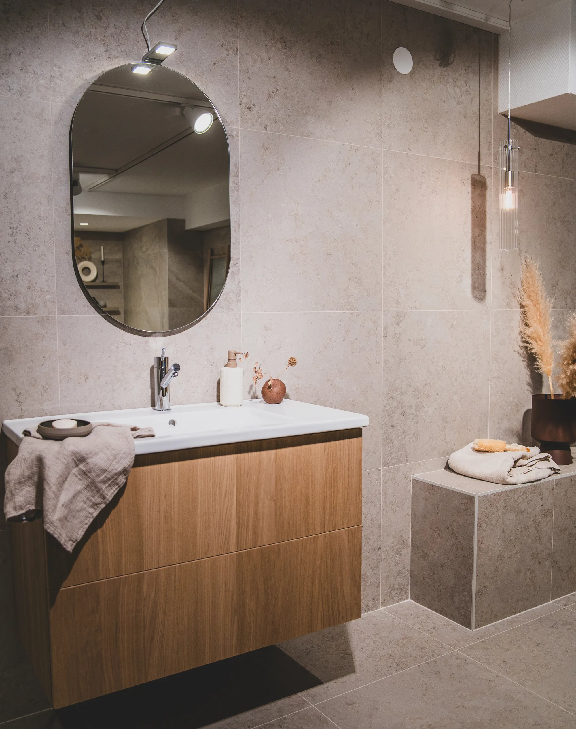 Golvabias badrumsinredning med träkommod, rund spegel och kaklade väggar.