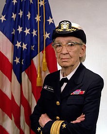 Grace Hopper i uniform med amerikanska flaggan i bakgrunden